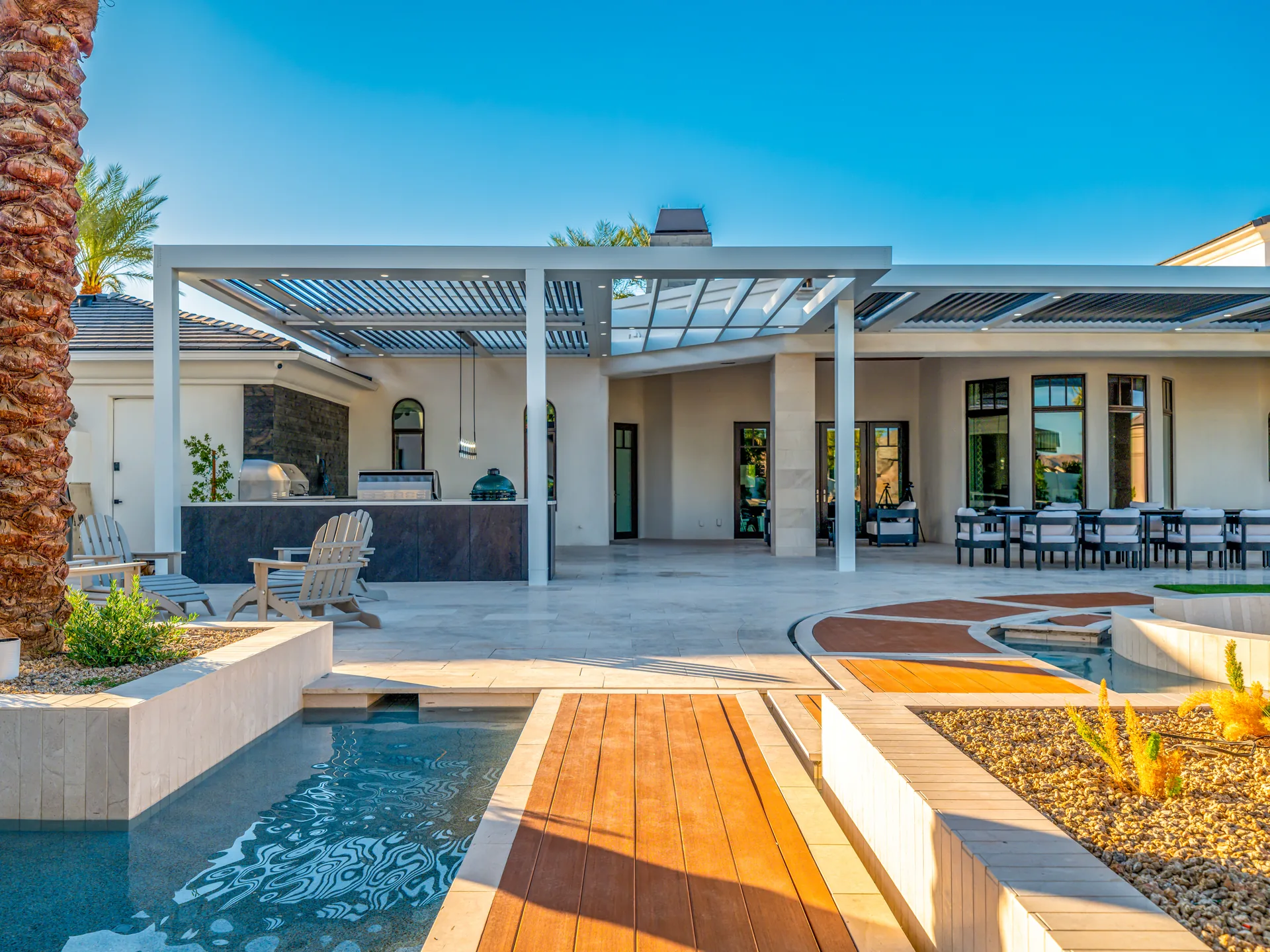 Wide louvered pergola covering a rear patio beside a raised wood deck, illustrating a shaded backyard retreat